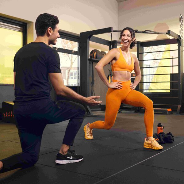 Personal Trainer supporting lady in orange outfi doing lunges correctly